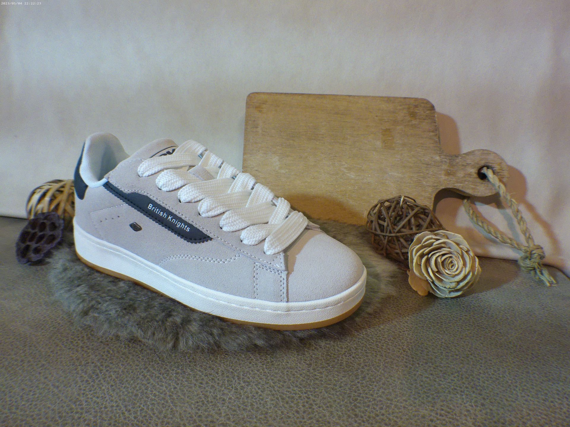 Een paar witte sneakers liggen op een tapijt naast een houten snijplank.