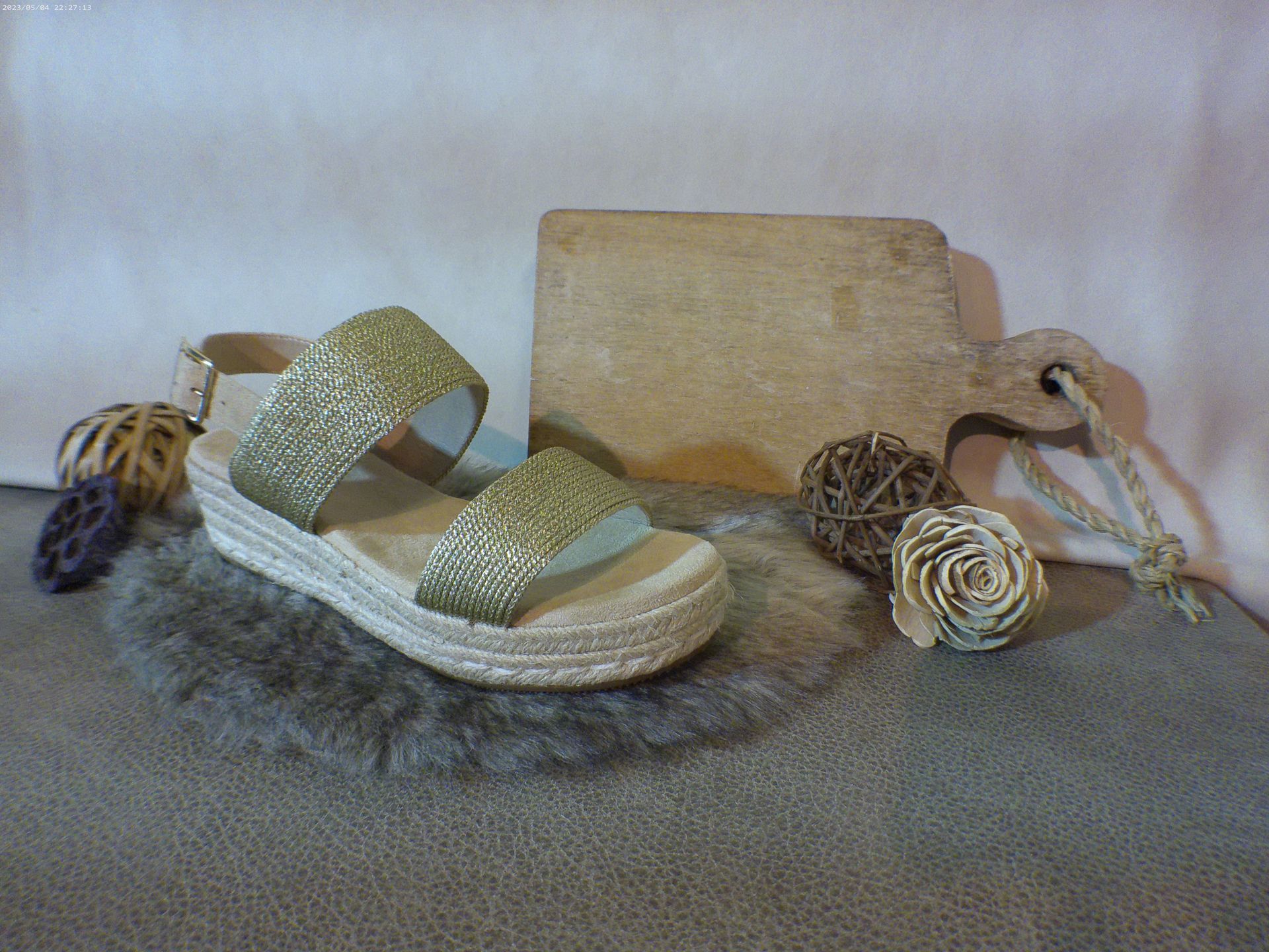 Een paar gouden sandalen liggen op een tapijt naast een houten snijplank.