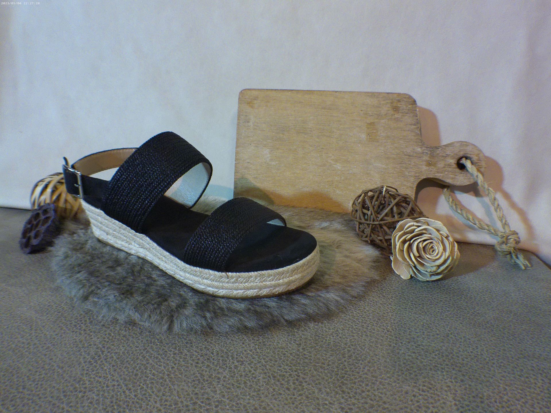 Een paar zwarte sandalen liggen op een tapijt naast een houten snijplank.