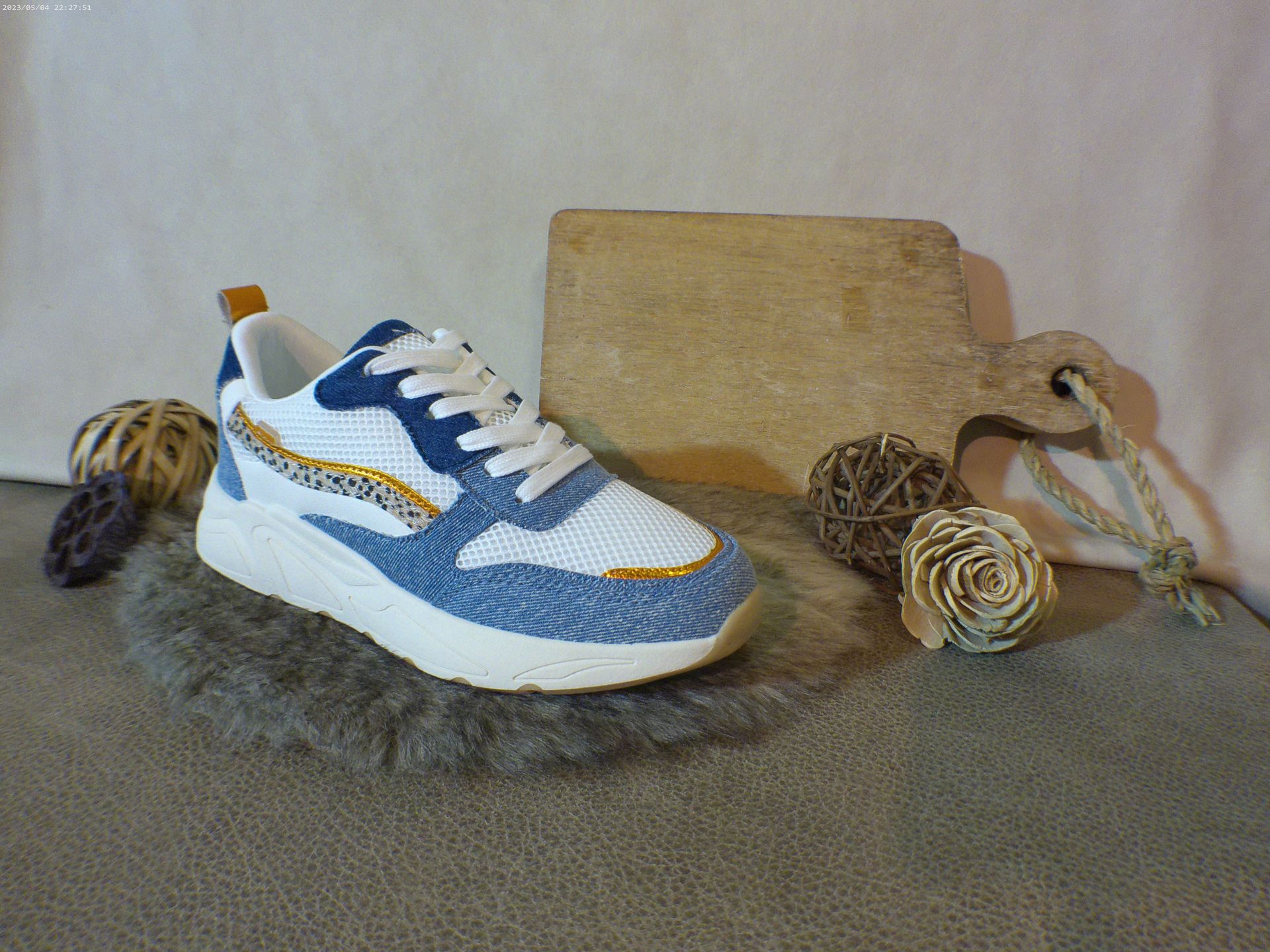Een paar blauw-witte sneakers liggen op een tapijt naast een houten snijplank.