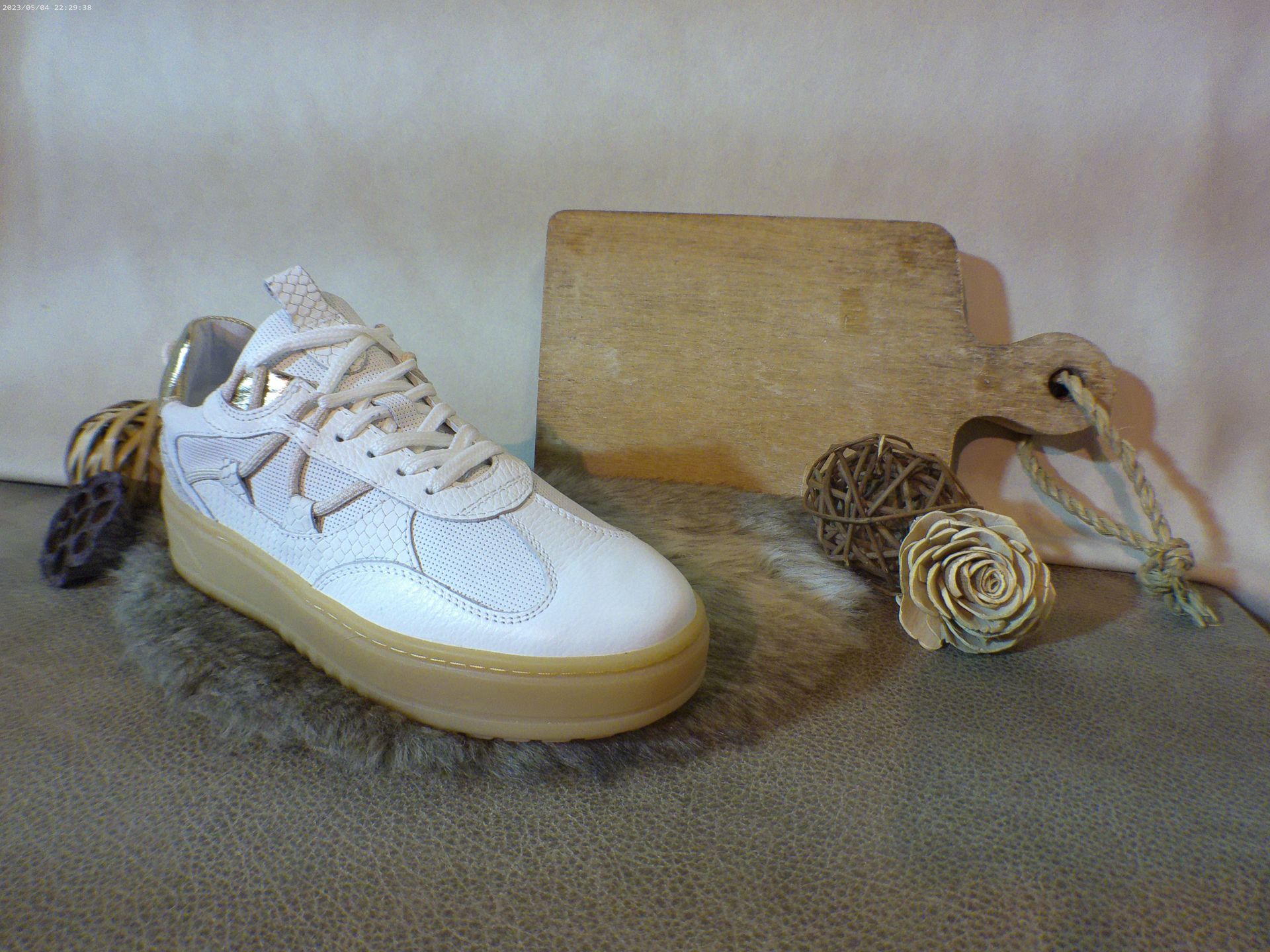 Een paar witte sneakers met een houten snijplank en bloemen op de achtergrond.