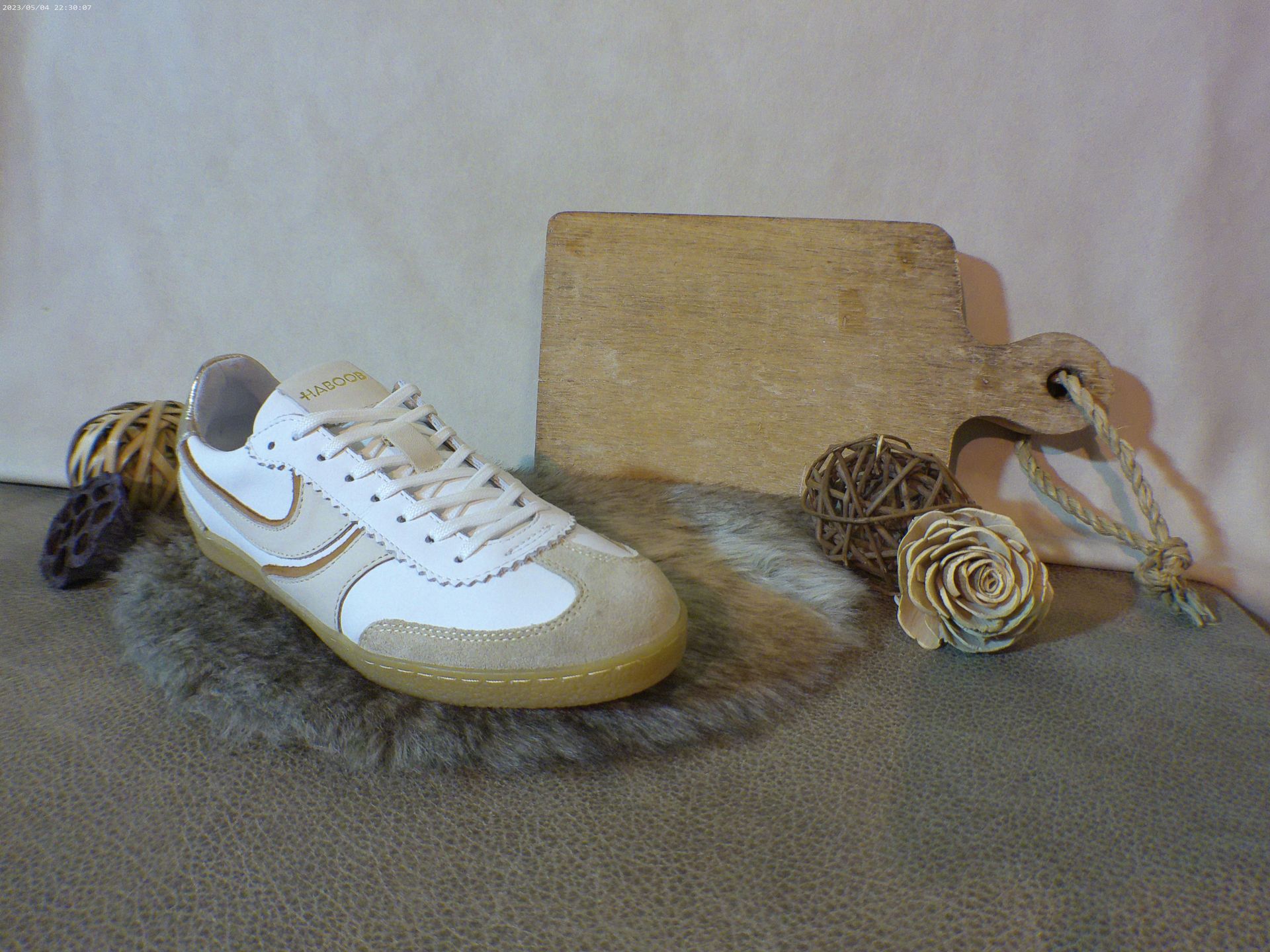 Een paar witte sneakers liggen op een tapijt naast een snijplank.