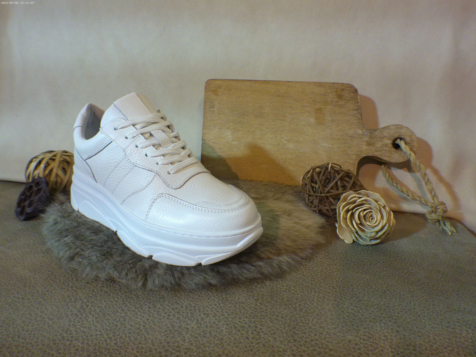 Een paar witte sneakers liggen op een tapijt naast een houten snijplank.