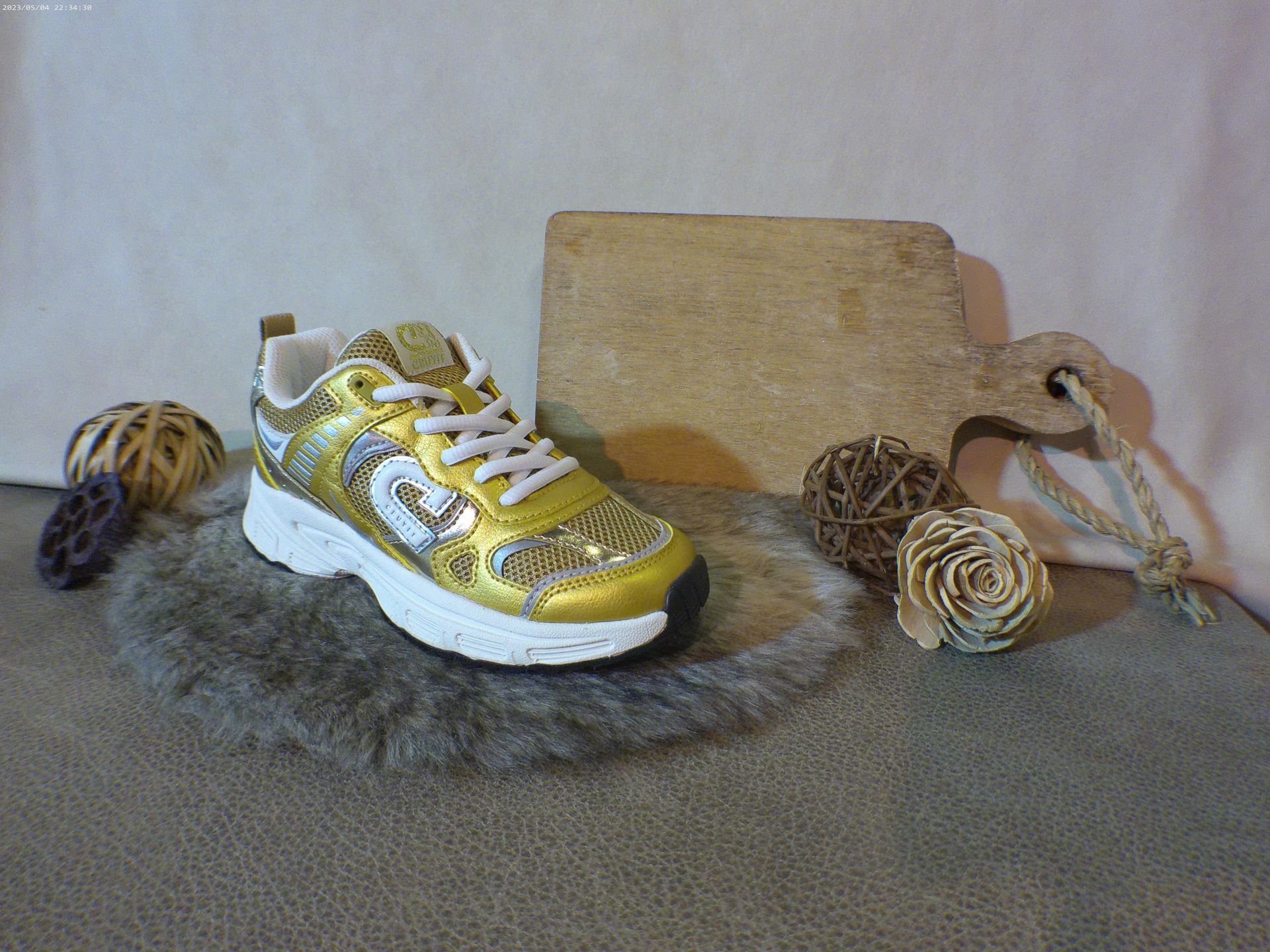 Een paar gouden sneakers liggen op een bontkleed.