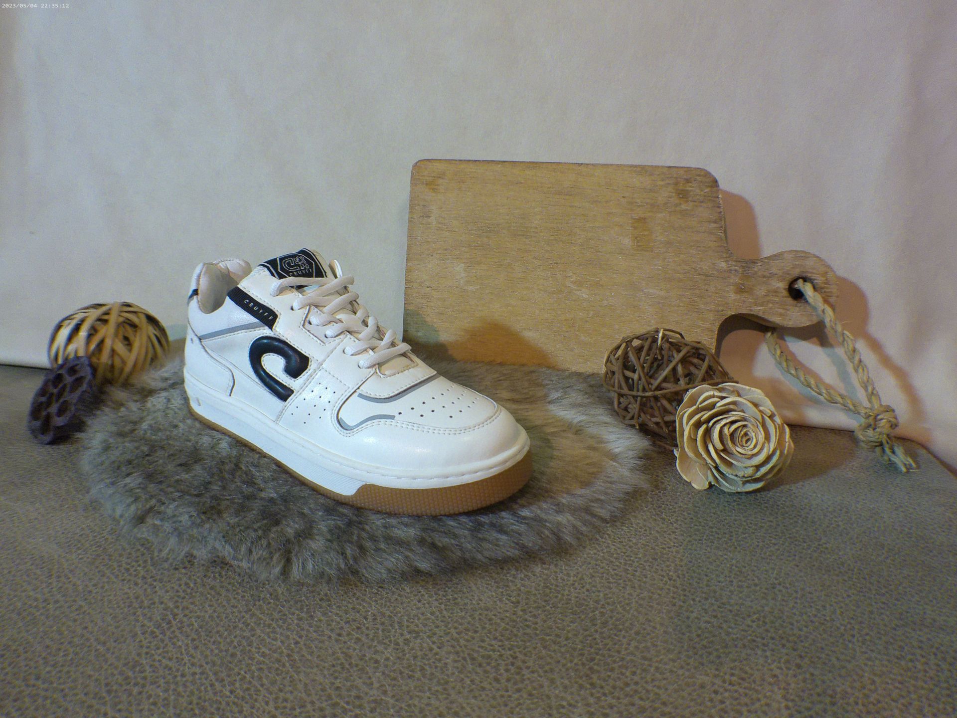 Een paar witte sneakers liggen op een tapijt naast een snijplank.