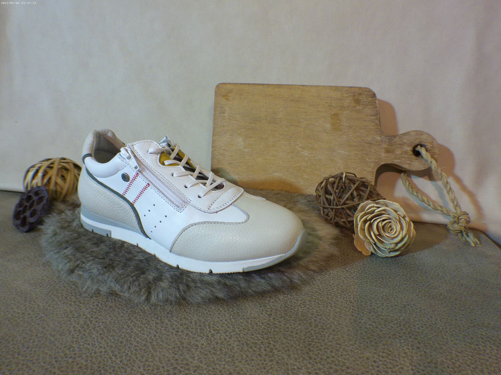 Een paar witte sneakers liggen op een tapijt naast een snijplank.