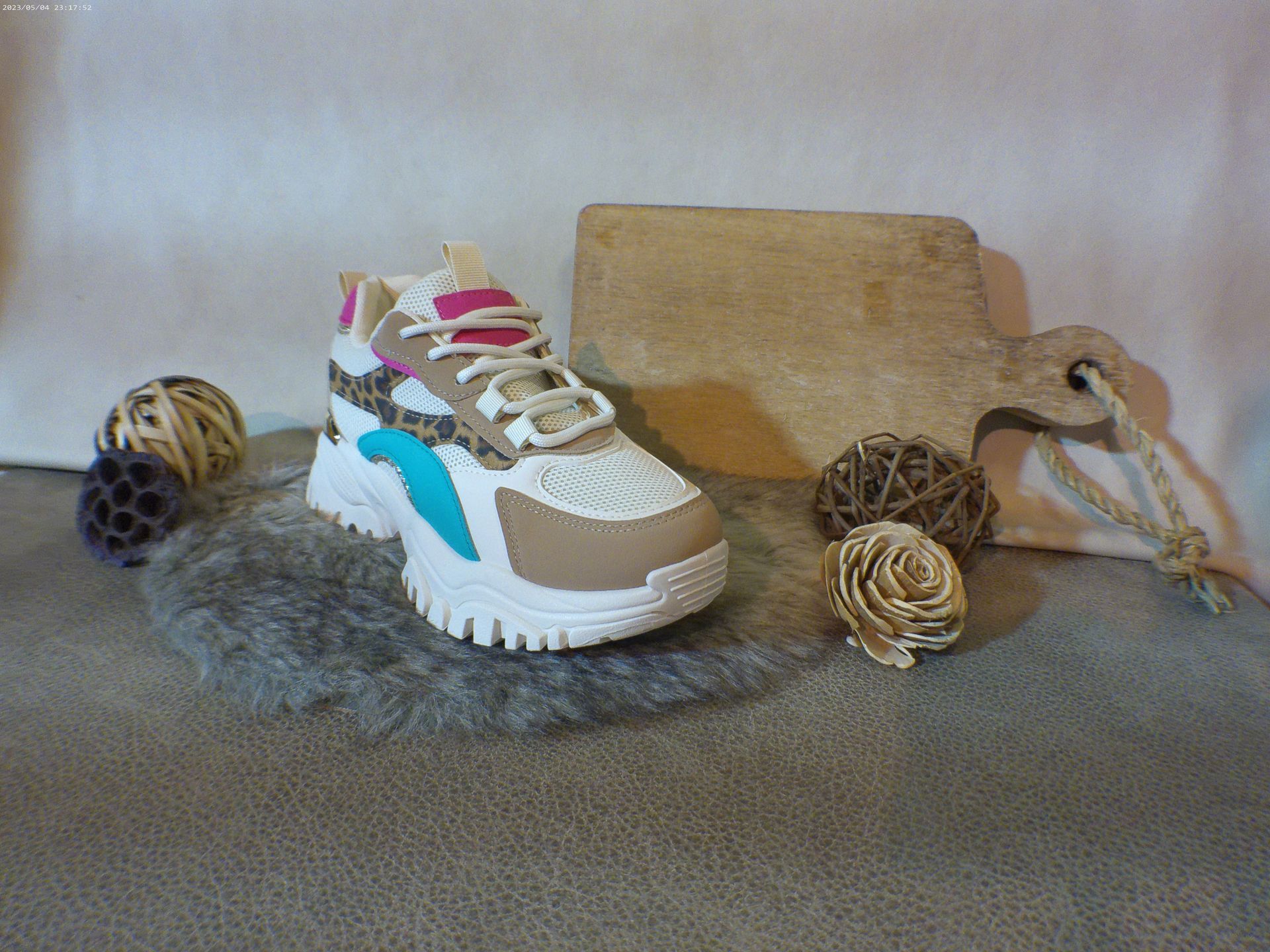 Een paar sneakers liggen op een tapijt naast een houten snijplank.