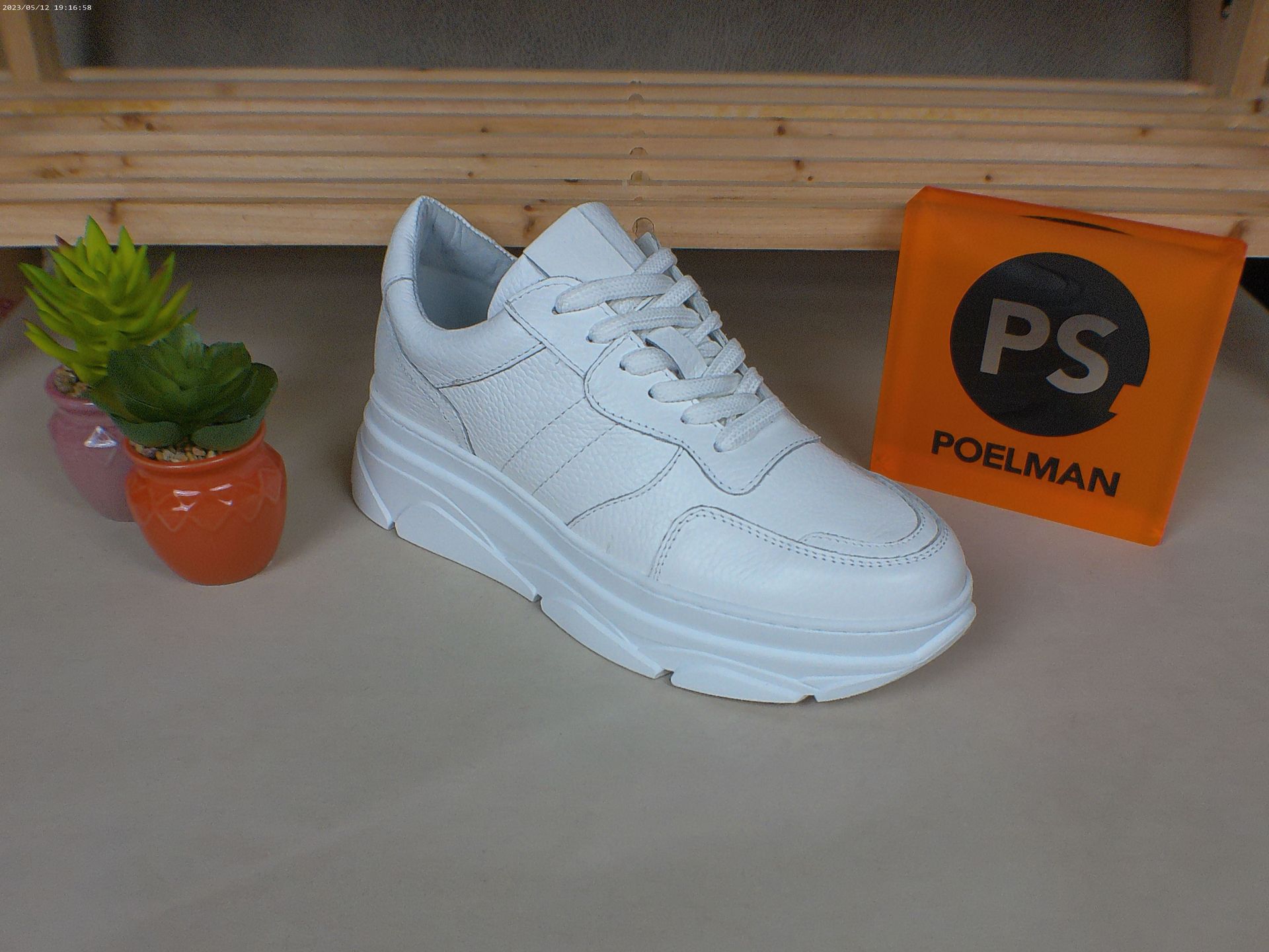 Een paar witte sneakers staan ​​op een tafel naast een potplant.