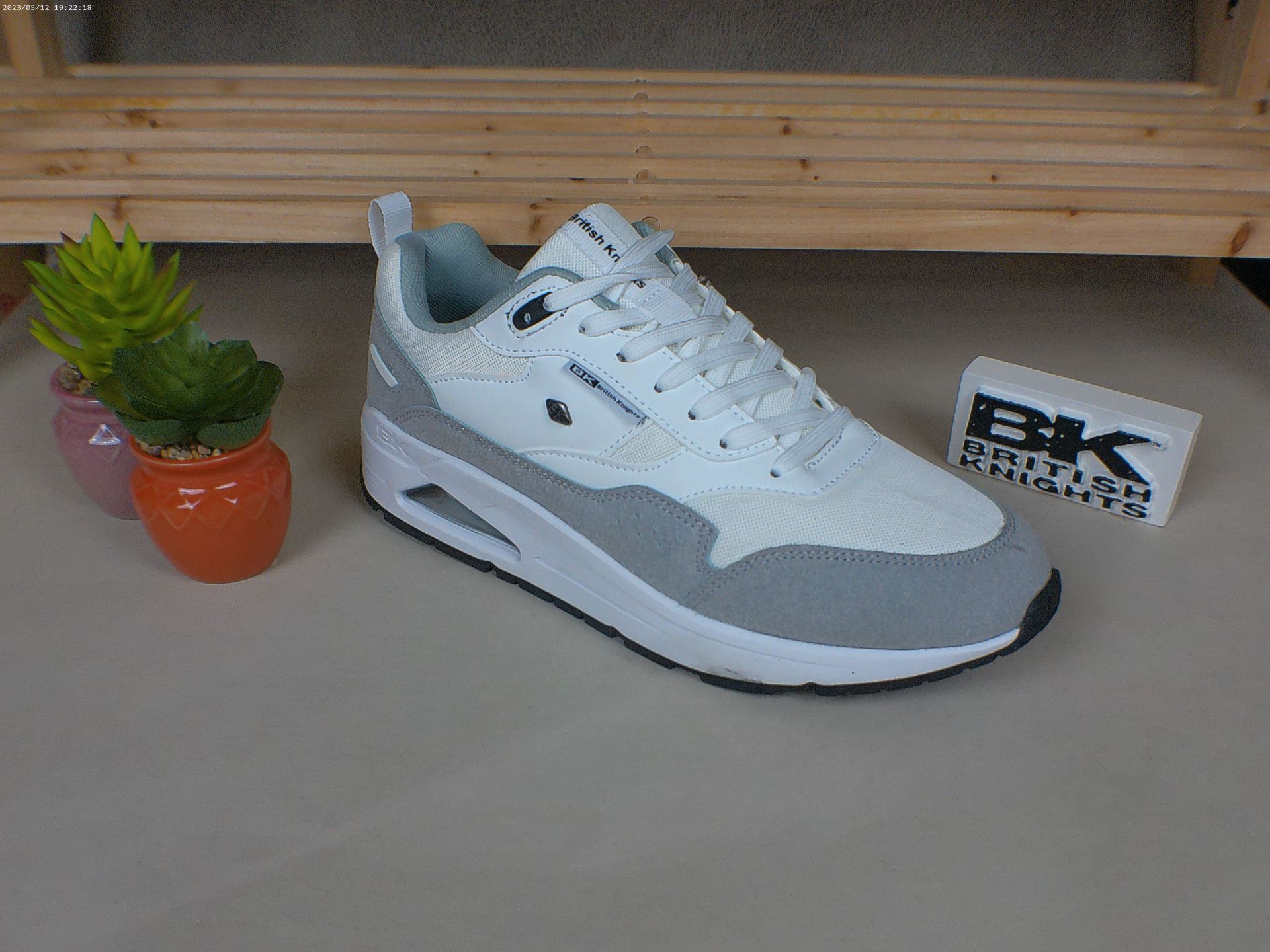 Een paar wit-grijze sneakers staan ​​op een tafel naast een potplant.