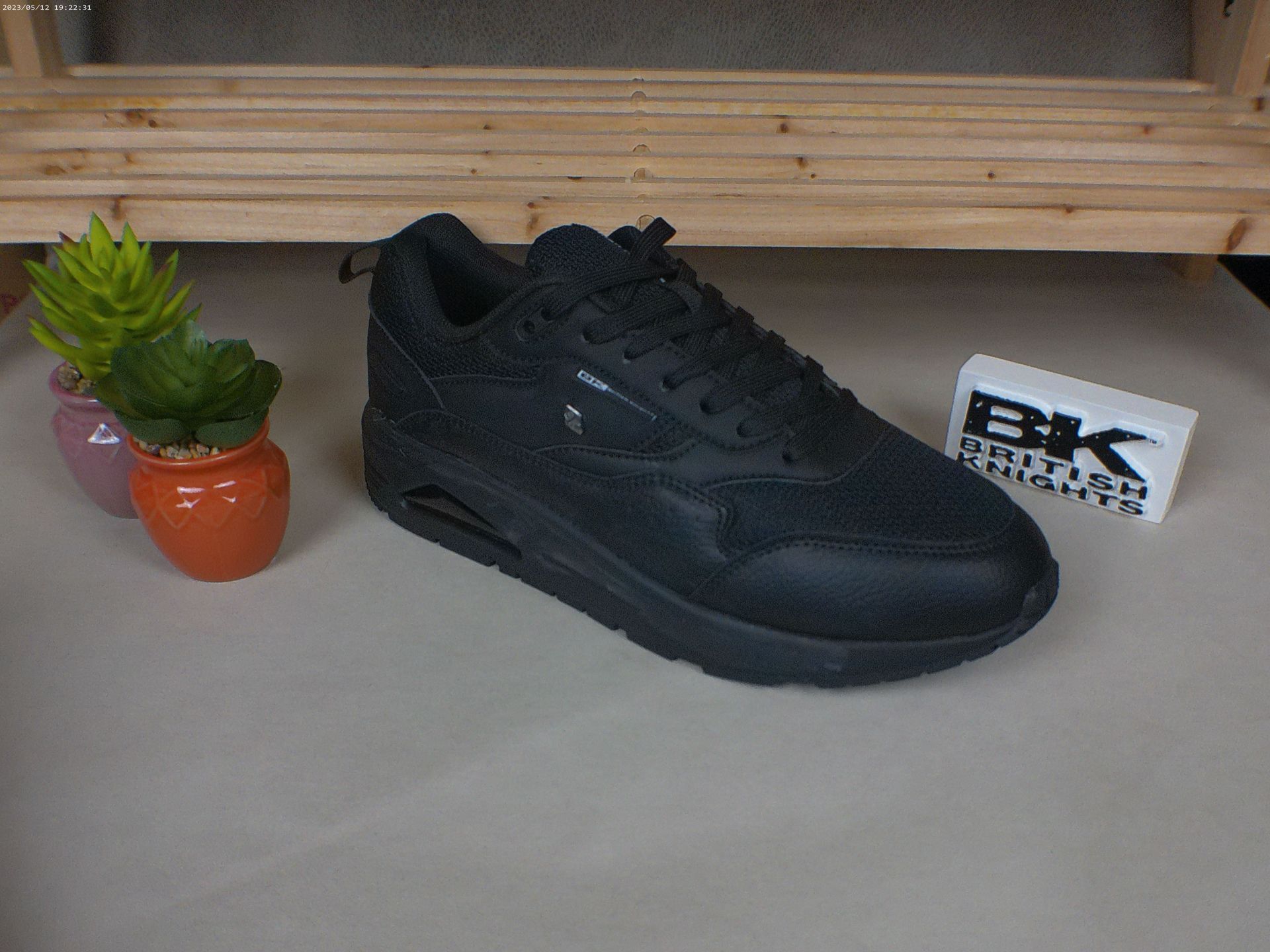 Een paar zwarte sneakers staan ​​op een tafel naast potplanten.