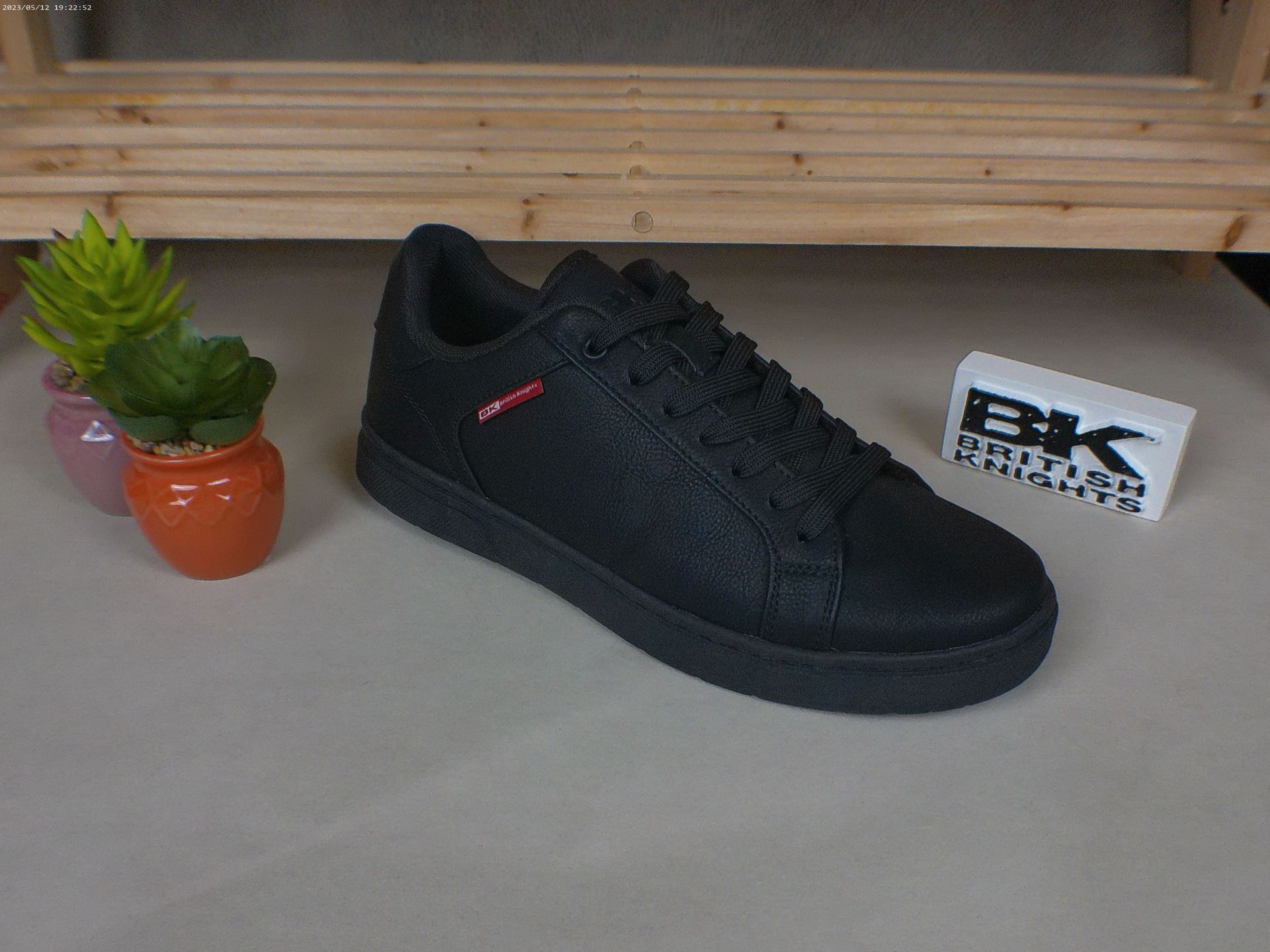 Een paar zwarte sneakers staan ​​op een tafel naast een potplant.