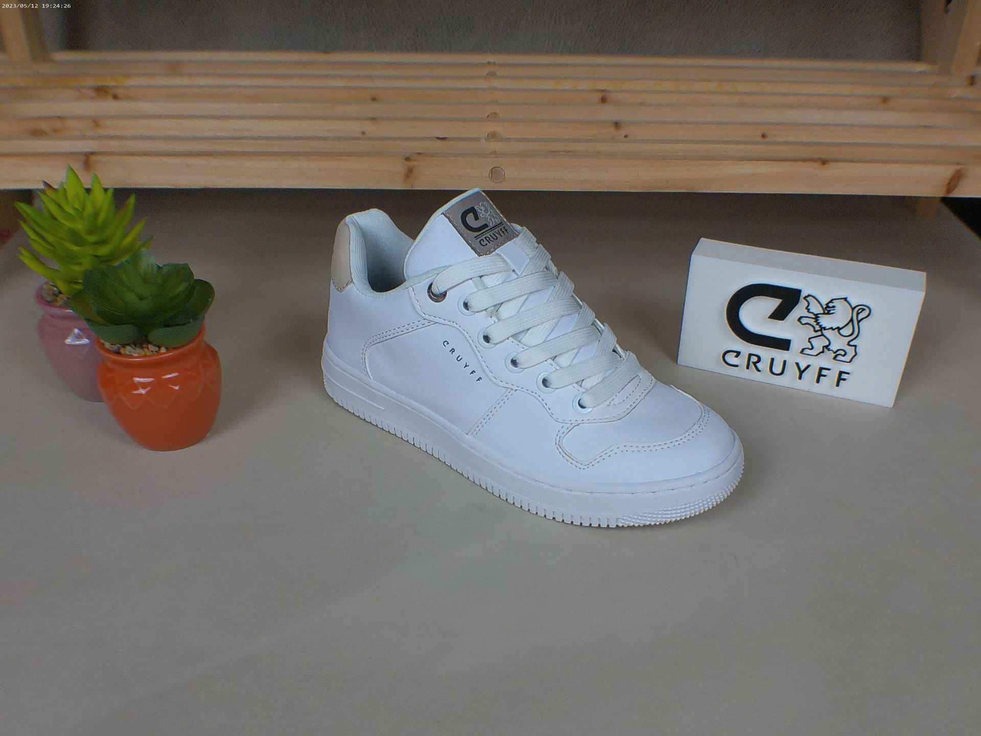 Een paar witte Cruyff-sneakers staan ​​op een tafel naast een potplant.
