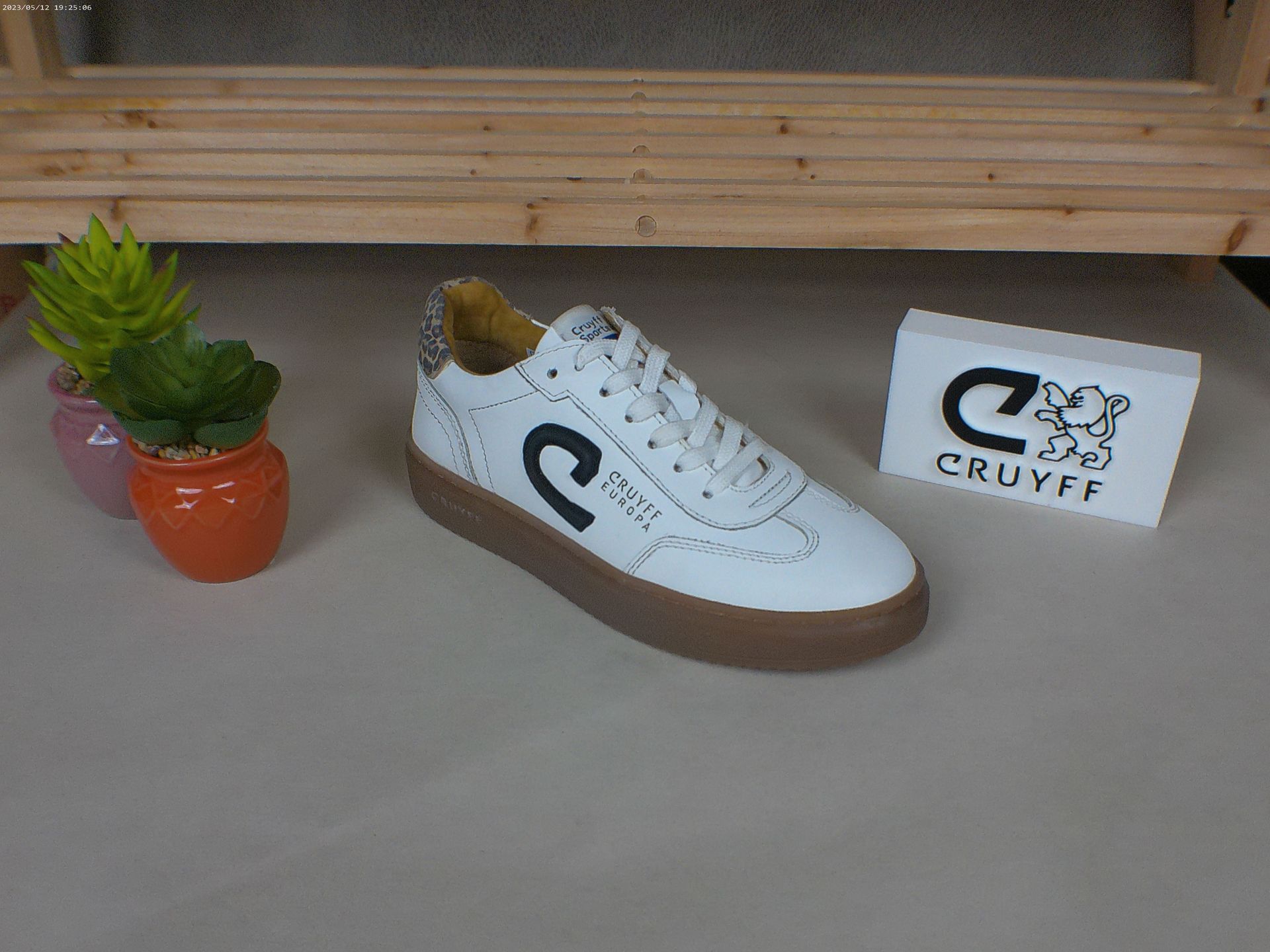 Een paar witte Cruyff-sneakers staan ​​op een tafel naast een potplant.