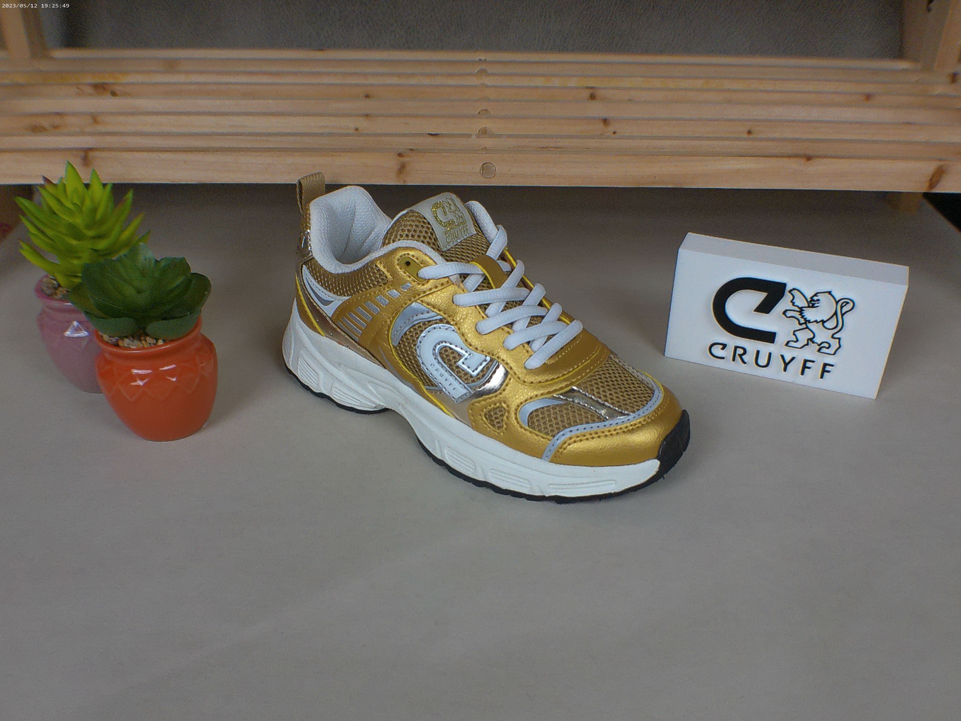 Een paar gouden en witte Cruyff-sneakers op een tafel
