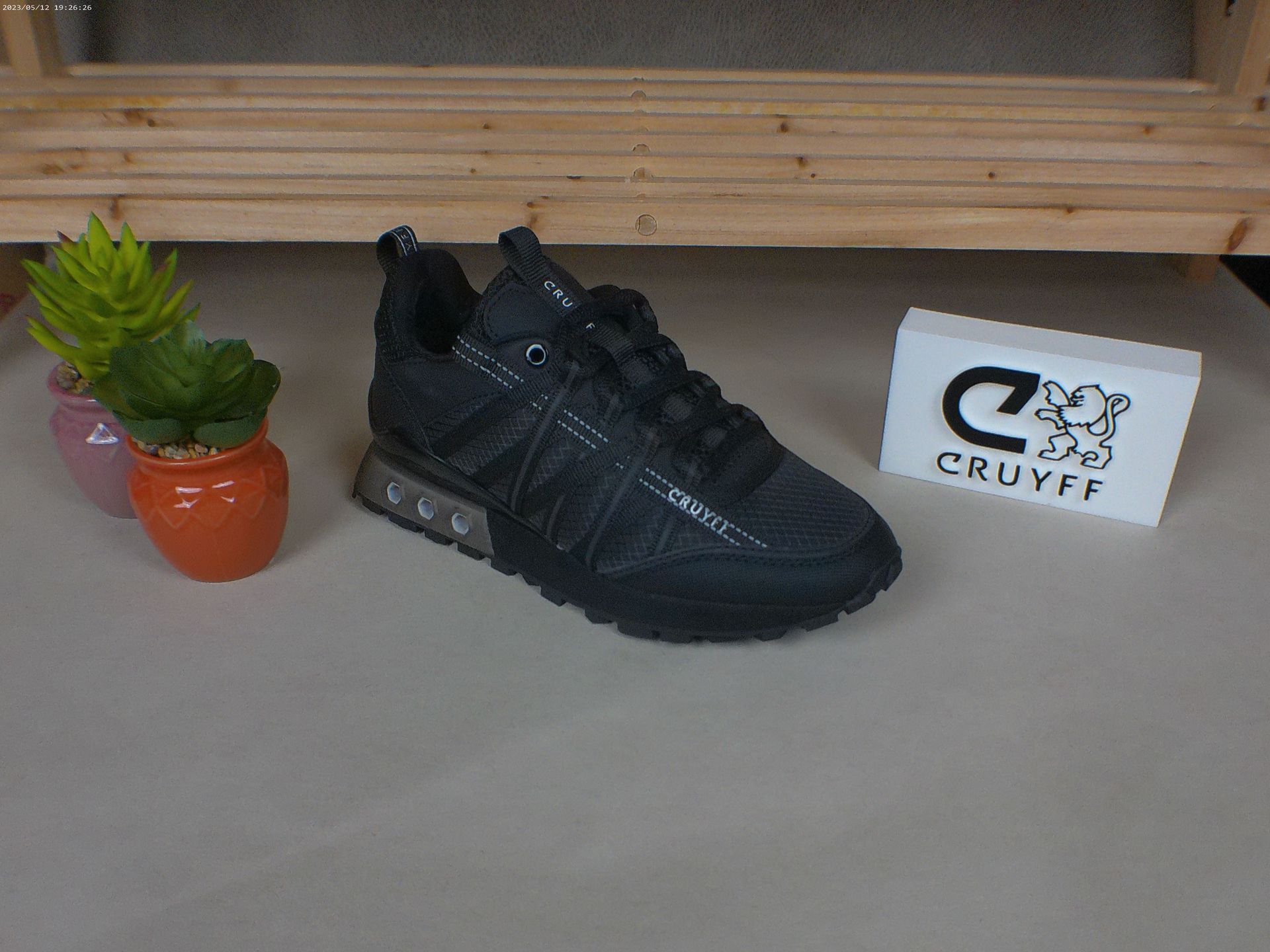 Een paar zwarte Cruyff-sneakers staan ​​op een tafel naast een potplant.