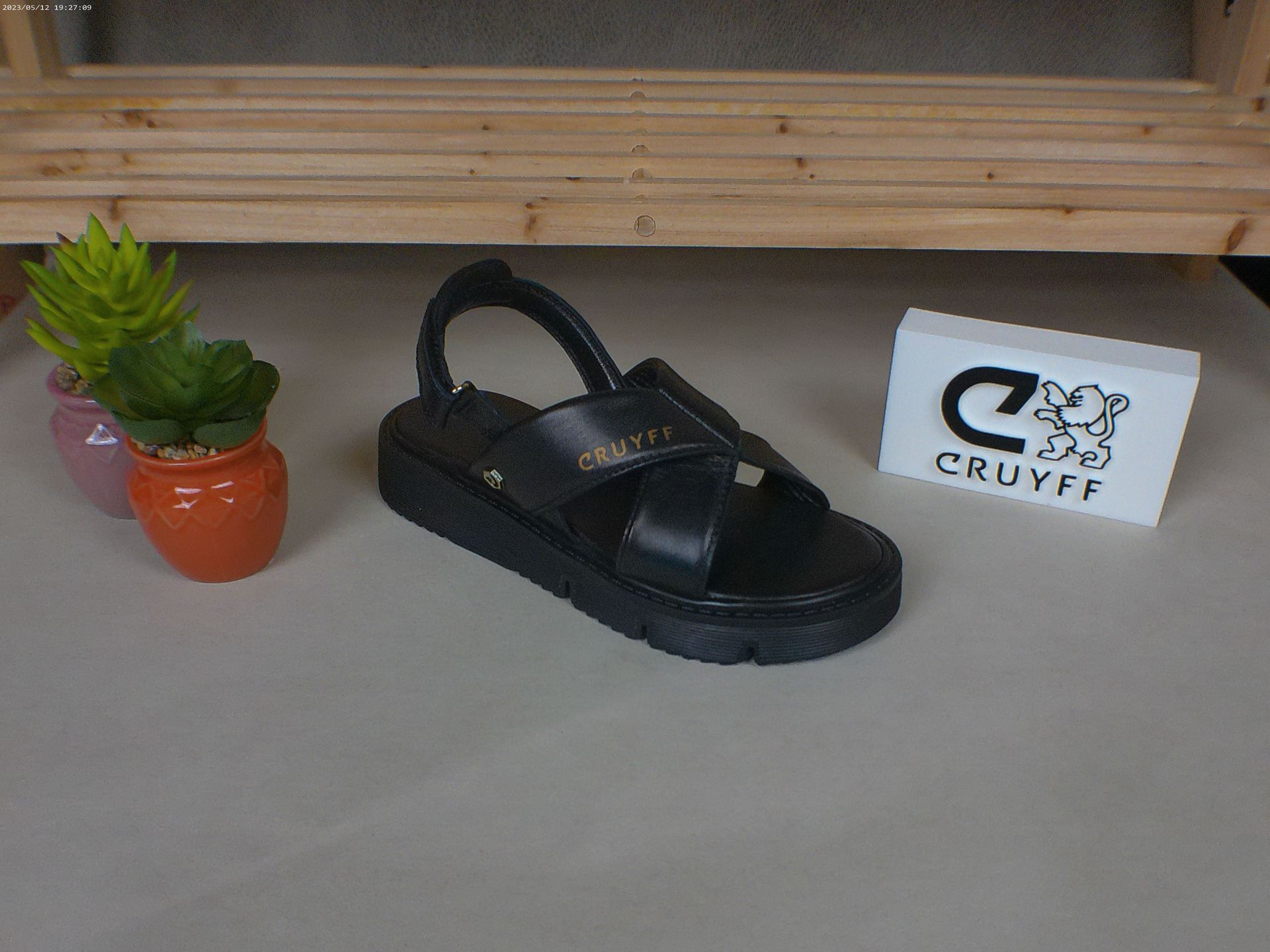 Een paar zwarte Cruyff-sandalen staan ​​op een tafel naast een potplant.
