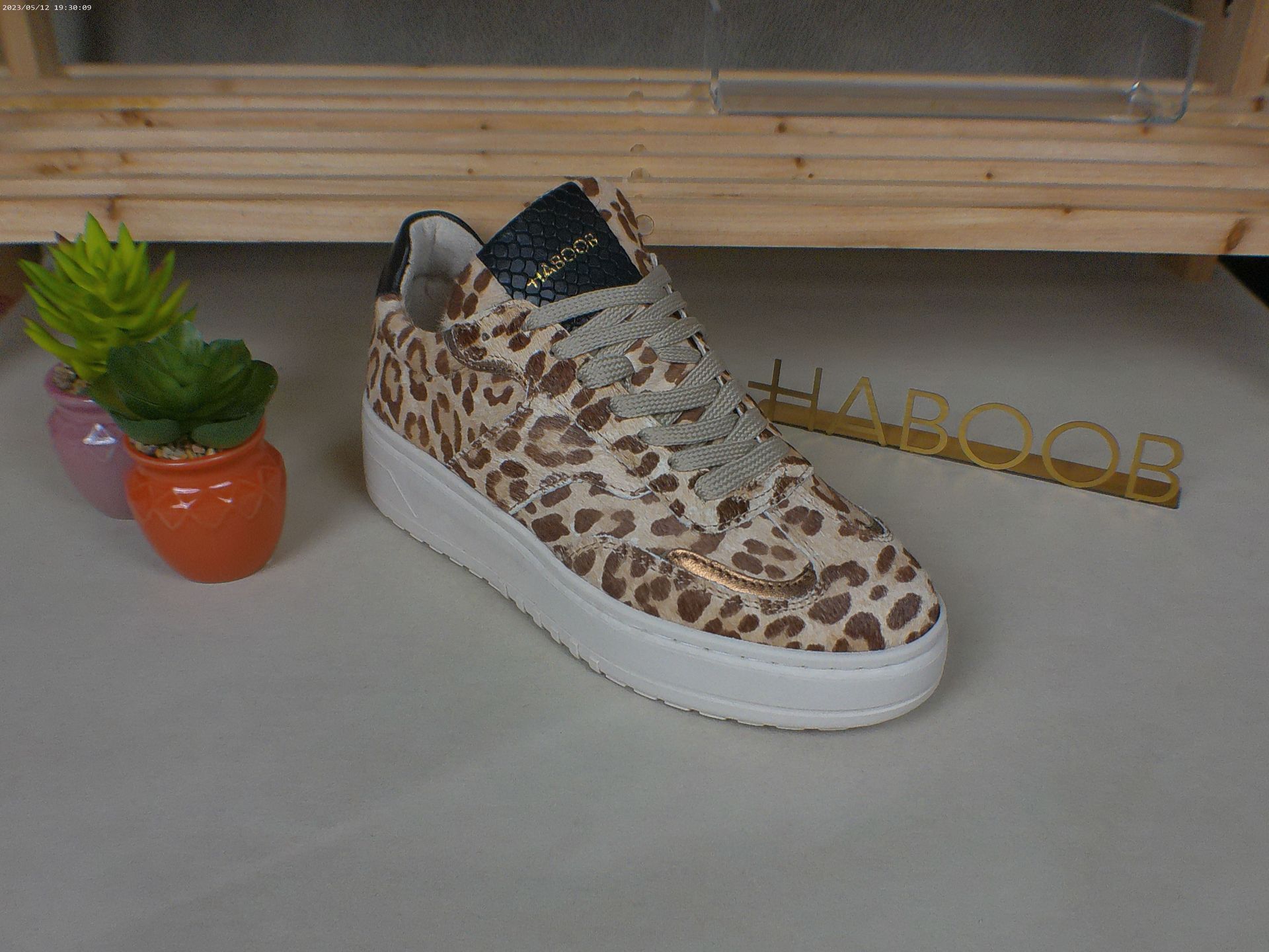 Een paar sneakers met luipaardprint staan ​​op een tafel naast een potplant.