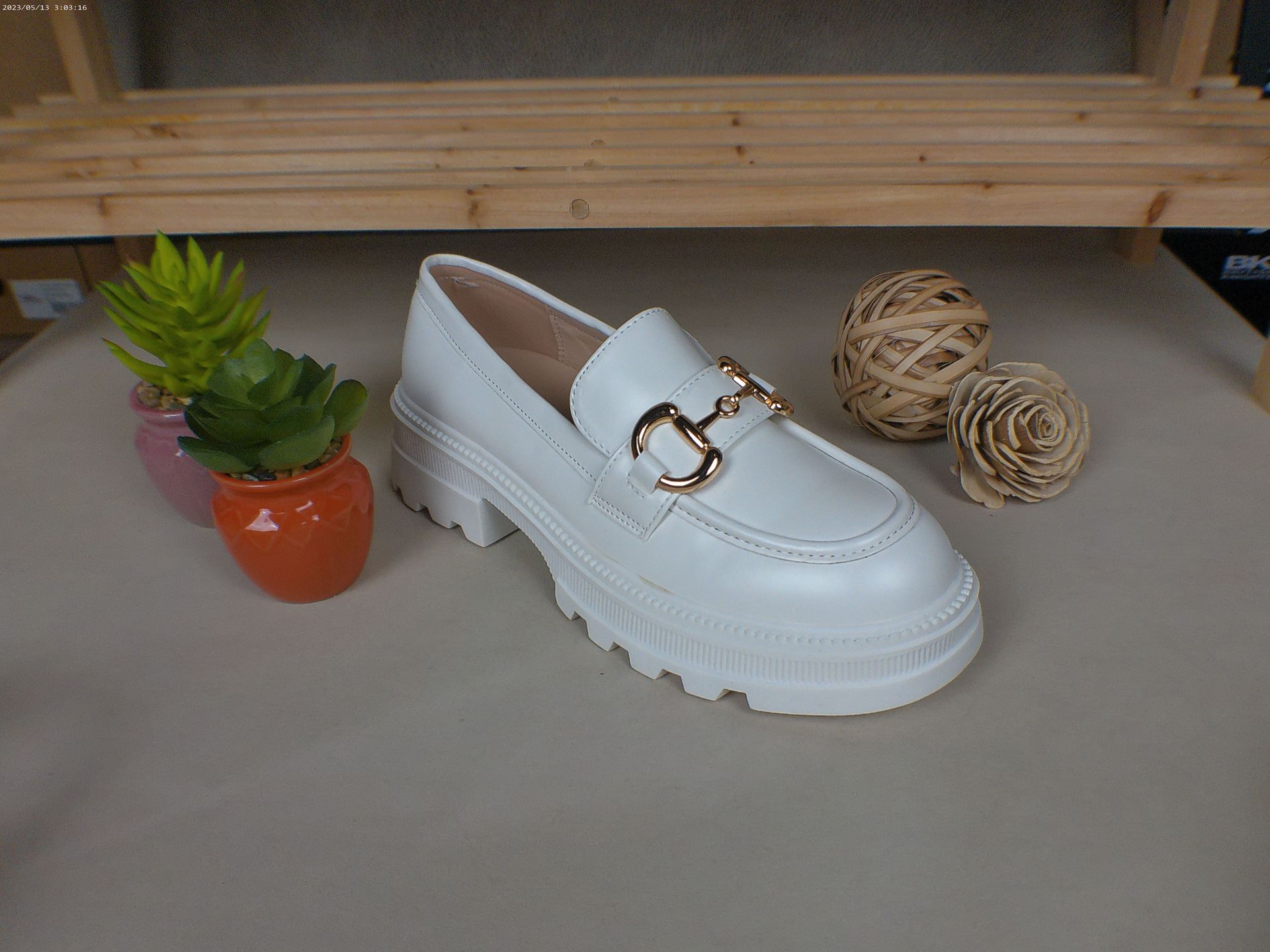 Een witte schoen met een gouden gesp staat op een tafel naast een potplant.