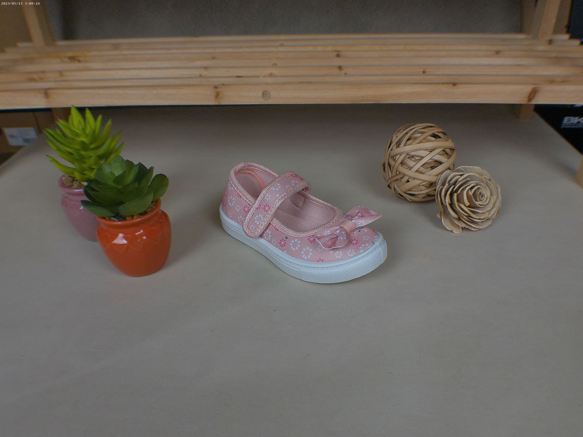 Een roze schoen staat op een tafel naast een potplant.