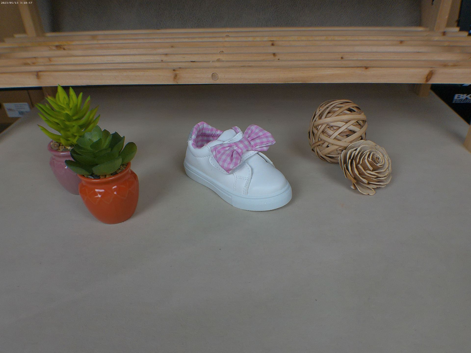 Een witte schoen met een roze strik staat op een tafel naast een potplant.