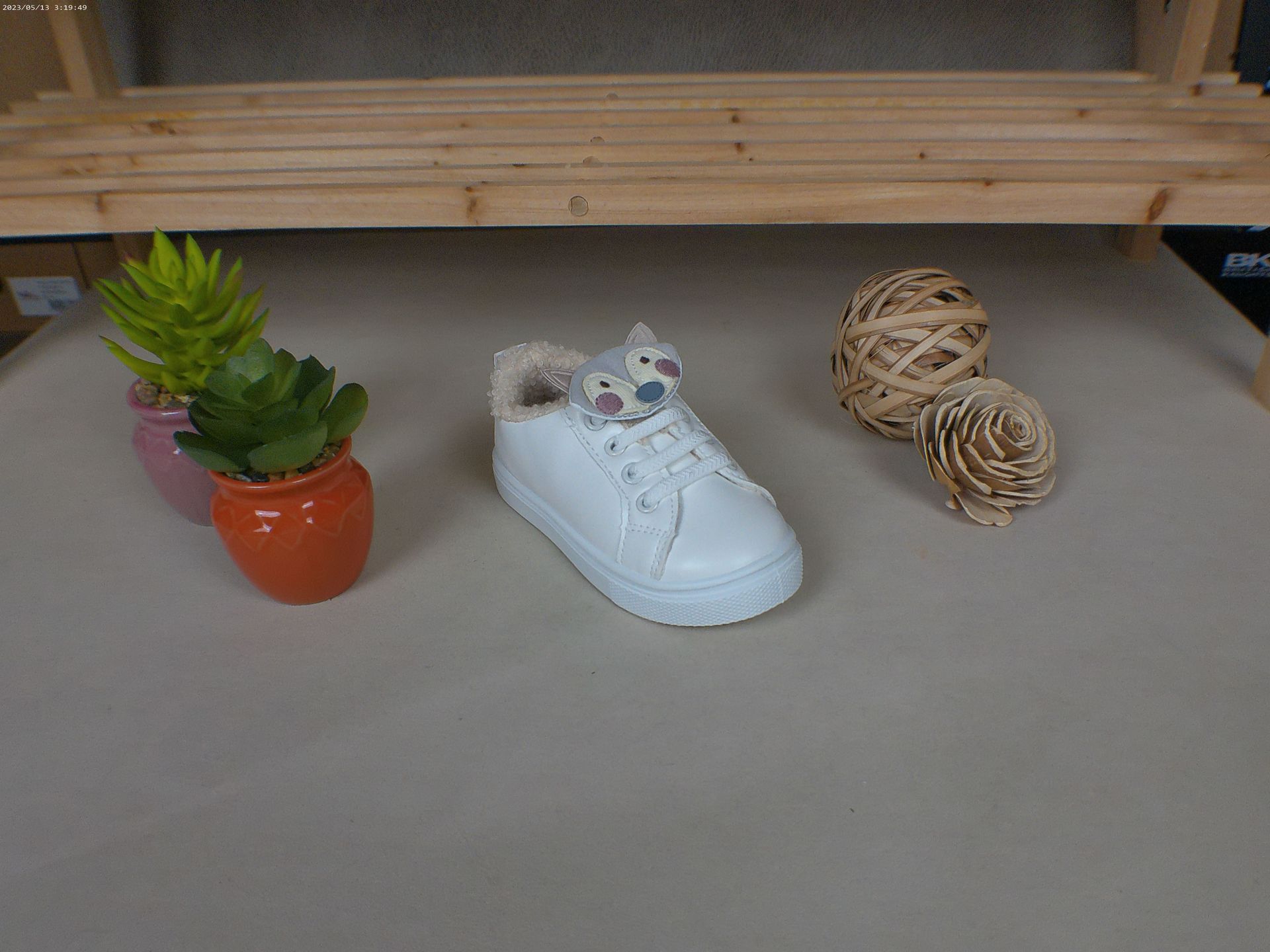 Een witte schoen met een kattengezicht erop staat op een tafel naast potplanten.