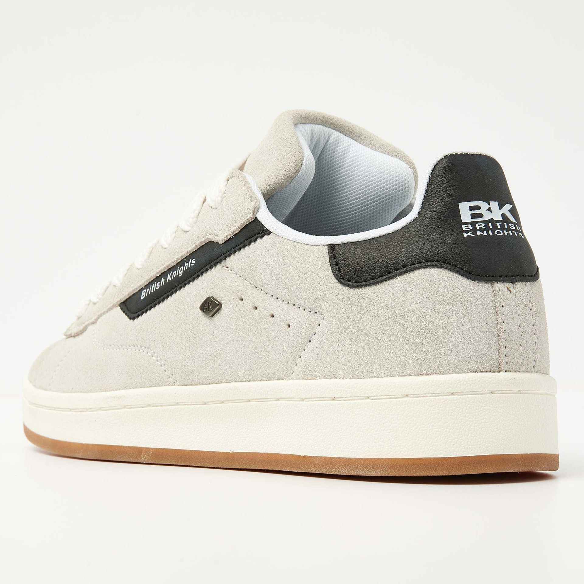 Beige suède sneaker met zwarte accenten, witte veters en bruine zool.