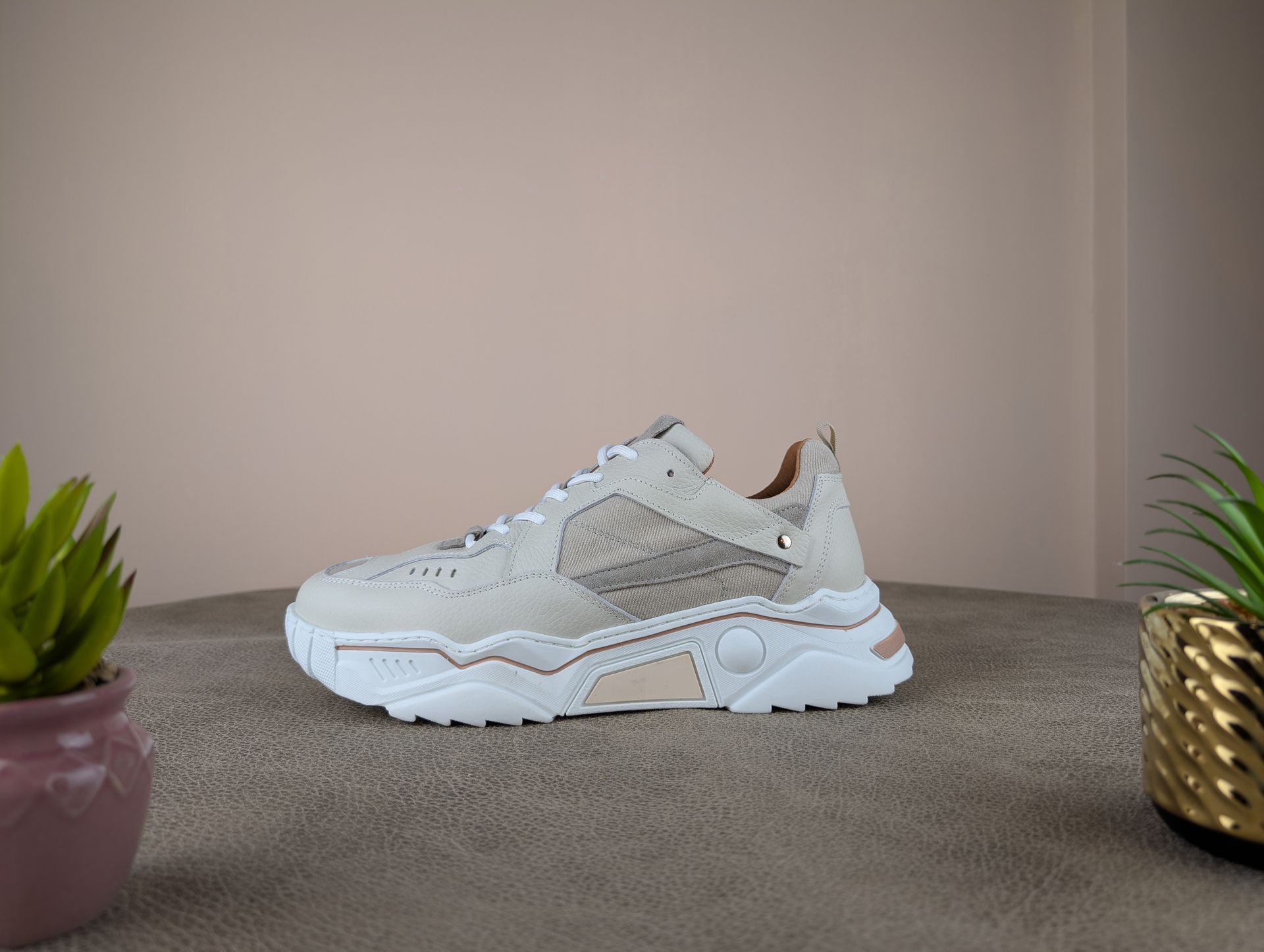 Beige en witte stevige sneakers op een bruin oppervlak, met twee kleine potplanten ernaast.