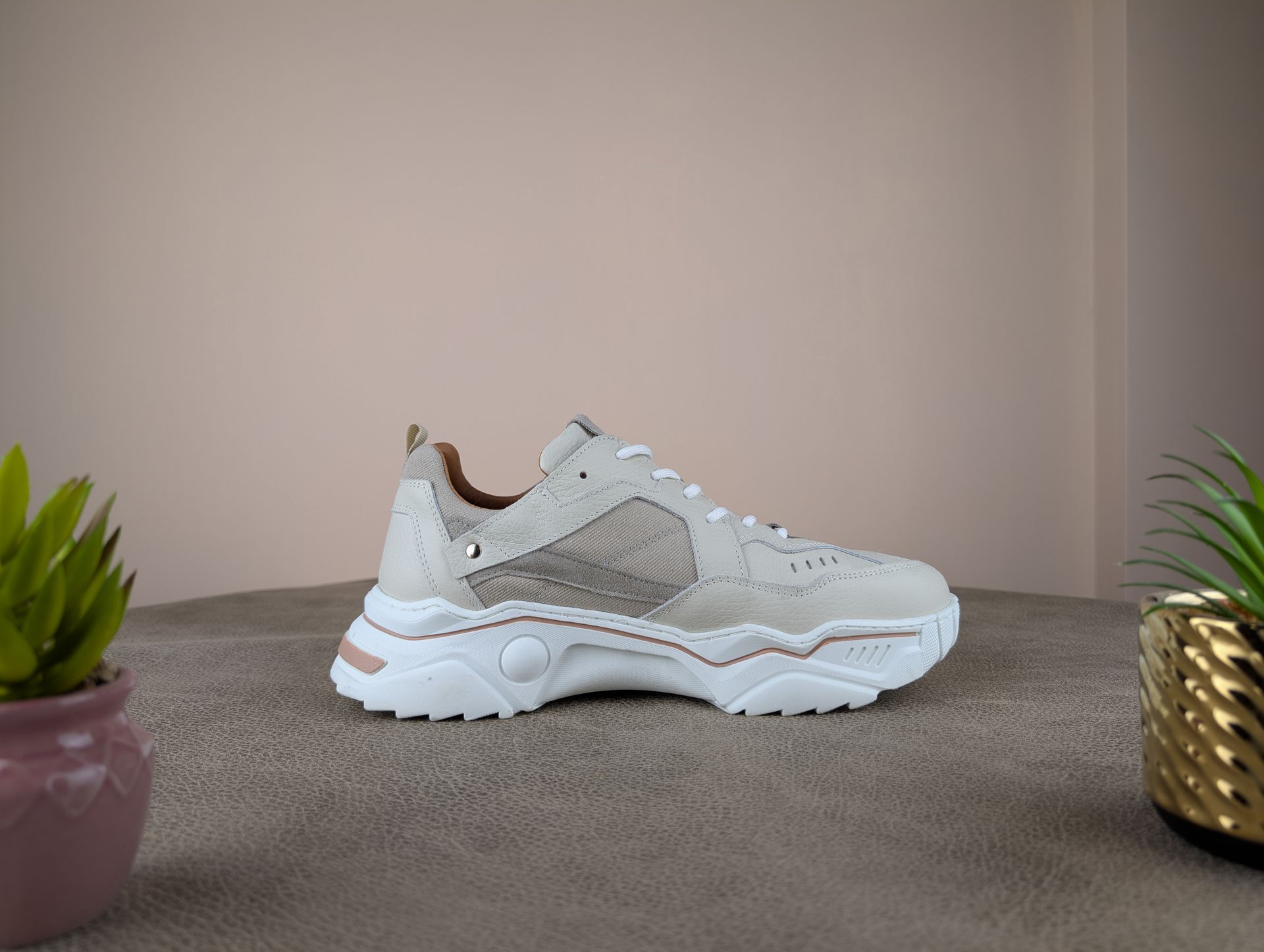 Beige en witte stevige sneakers op een bruin oppervlak, met twee kleine potplanten ernaast.