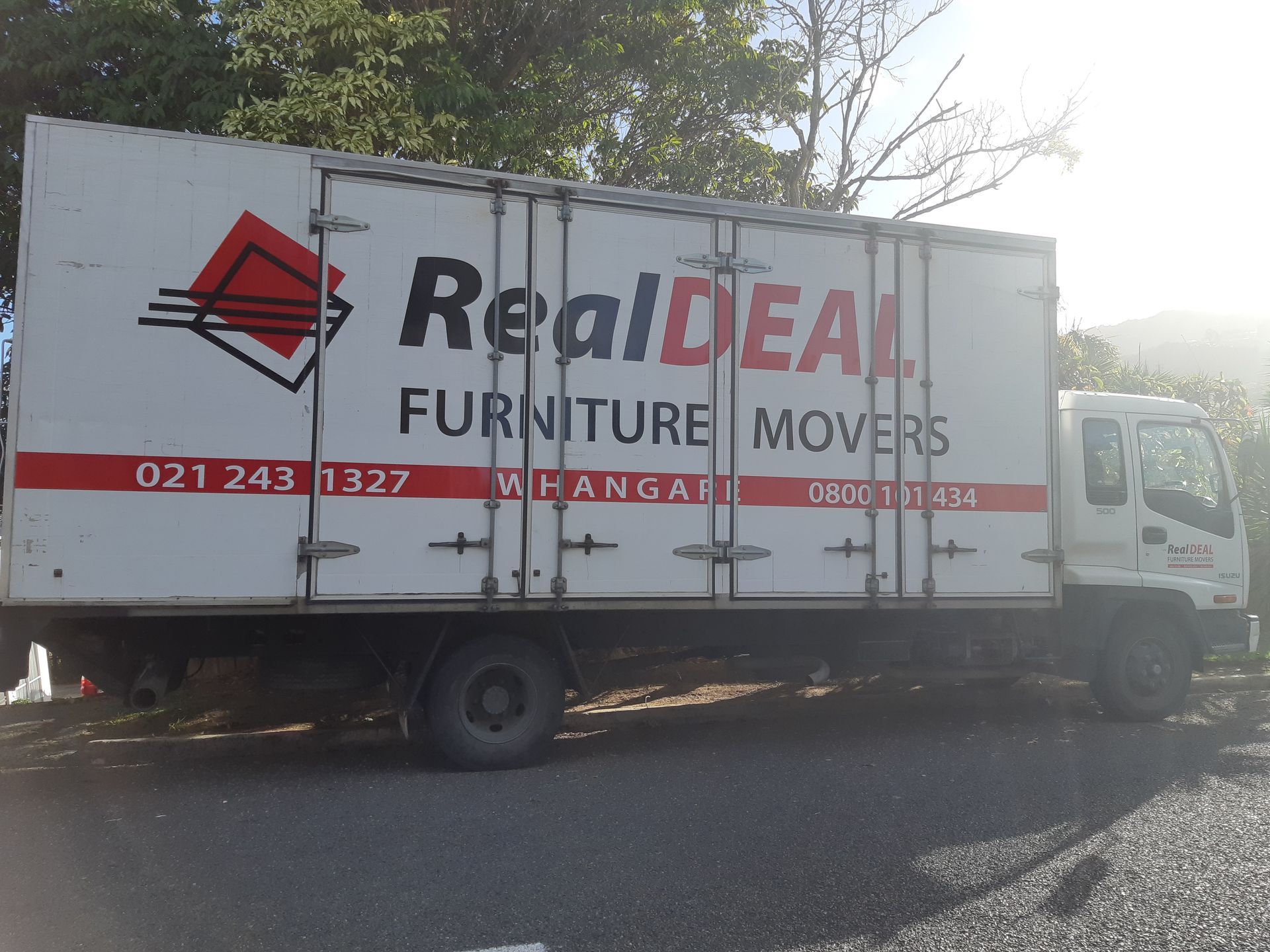 A Real Deal Furniture Movers truck is parked on the side of the road.