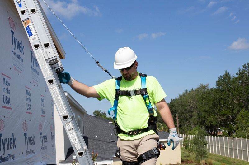 A man wearing a hard hat and safety harness is standing next to a ladder.