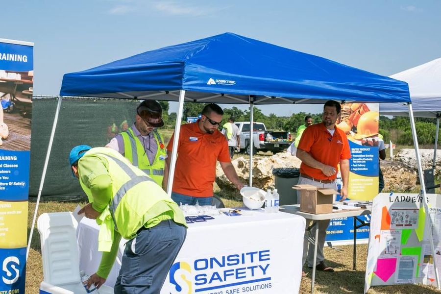 A group of men are standing around a table under a blue tent.