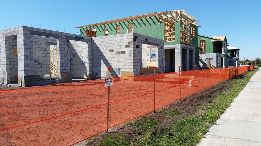 A house is being built next to a sidewalk and a fence.