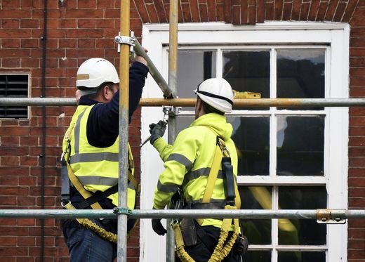 Two construction workers are working on a window on a scaffolding.