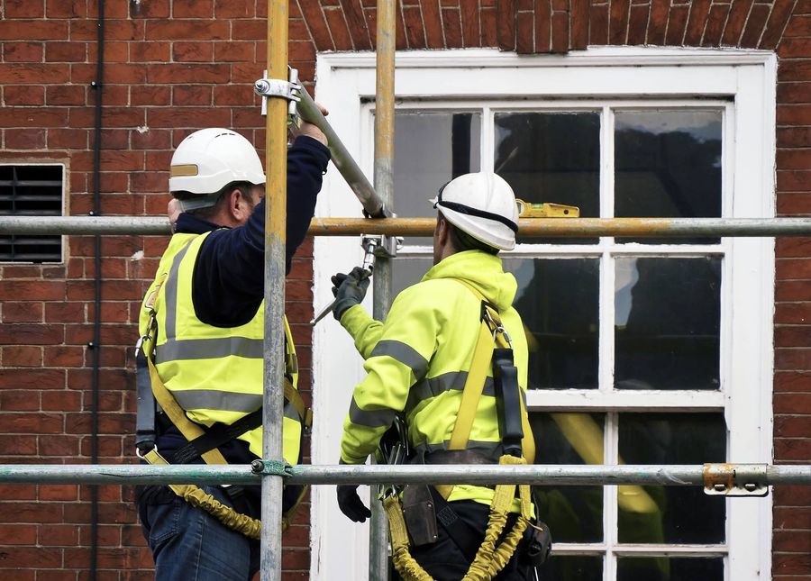 Two construction workers are working on a window on a scaffolding.