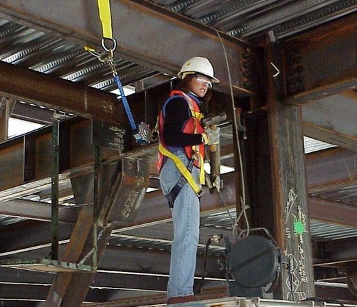 A woman wearing a hard hat and safety harness is working on a metal structure