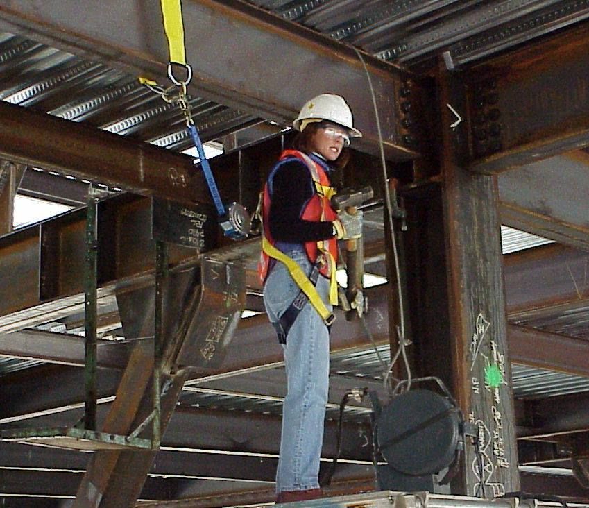 A woman wearing a hard hat and safety harness is working on a metal structure