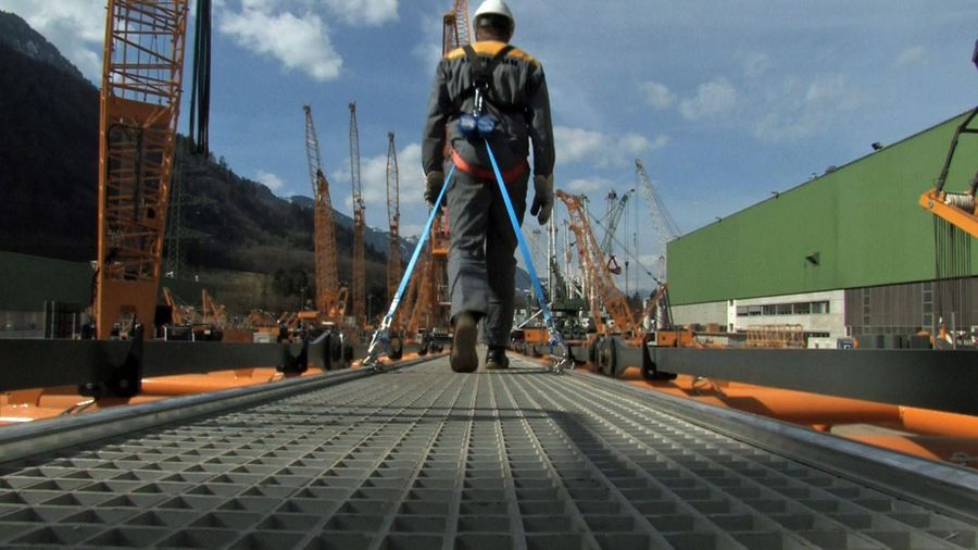 A man wearing a hard hat and safety harness is walking across a bridge.