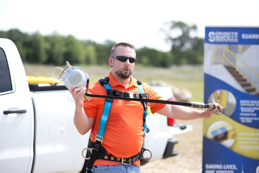A man wearing a safety harness is standing in front of a white truck.