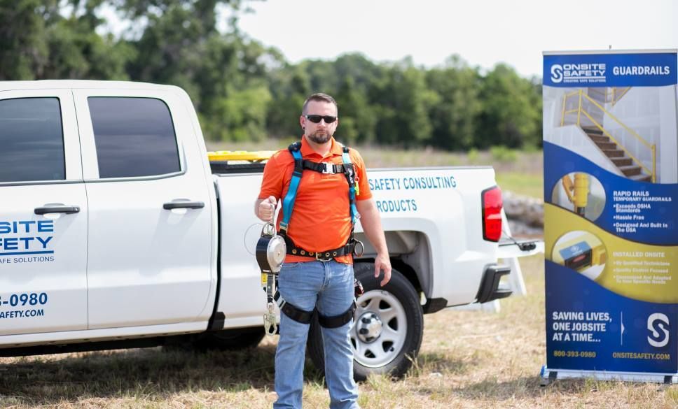 A man wearing a safety harness is standing in front of a white truck.