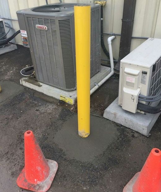 An air conditioner is sitting next to a yellow pole