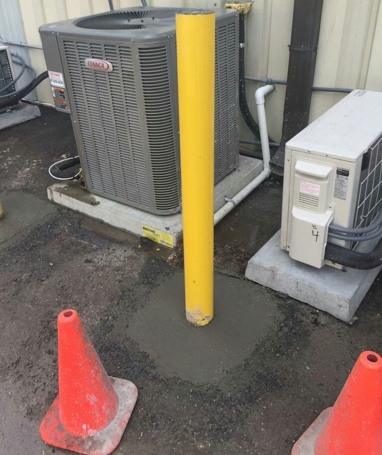 An air conditioner is sitting next to a yellow pole