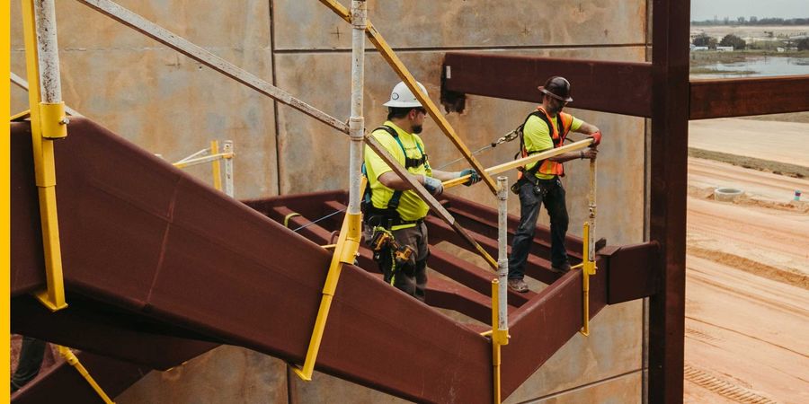 Two construction workers are standing on top of a metal staircase.