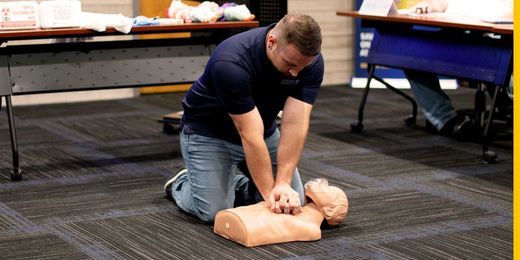 A man is kneeling on the floor doing a heart massage on a mannequin.