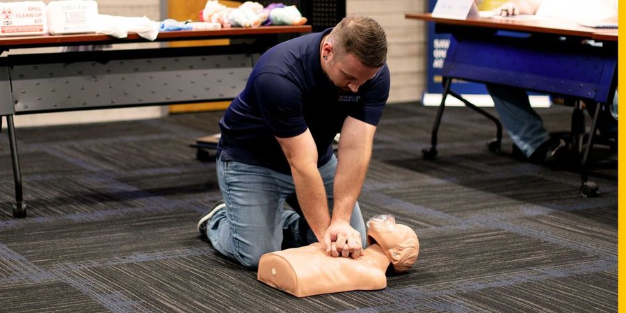 A man is kneeling on the floor doing a heart massage on a mannequin.