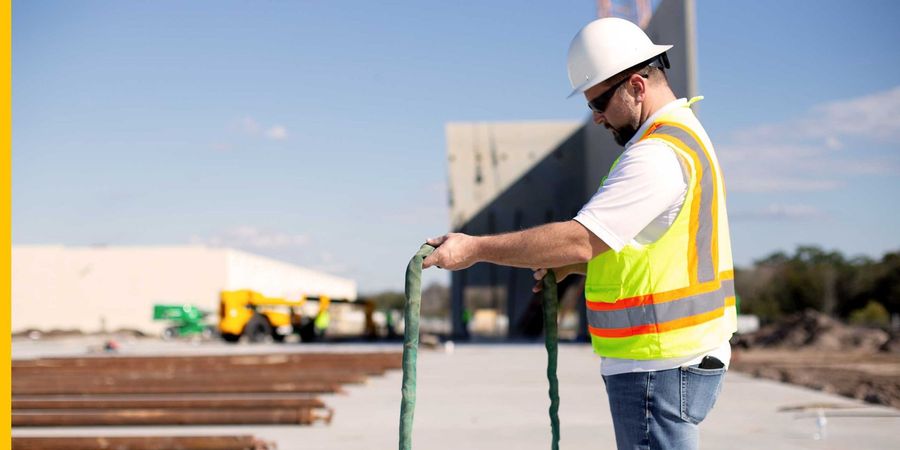 A construction worker wearing a hard hat and safety vest is pushing a cart.