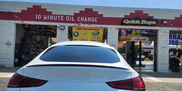 A white car is parked in front of a 10 minute oil change | Quick Boys Brake & Tune