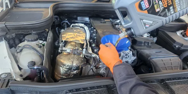 A person is pouring oil into a car engine | Quick Boys Brake & Tune