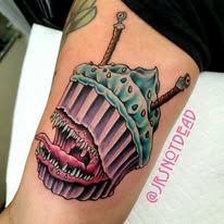 A tattoo of a cupcake with sharp teeth on a person 's arm.
