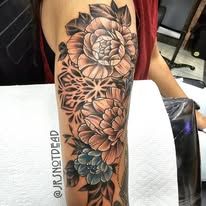 A woman has a tattoo of flowers and a mandala on her arm.