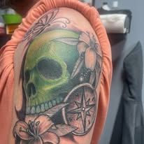 A woman has a tattoo of a skull with flowers and a compass on her shoulder.